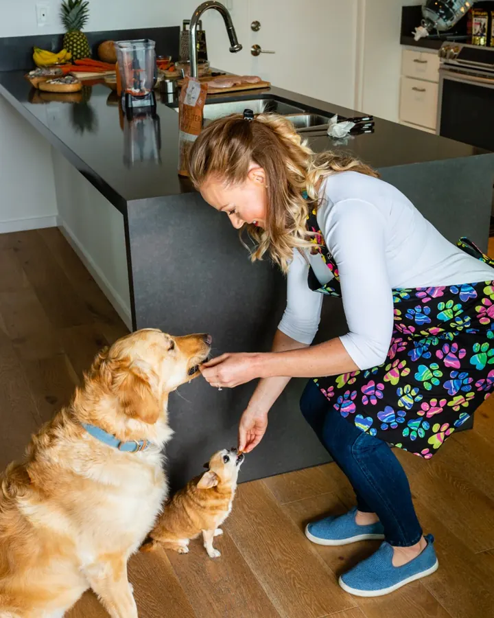 Melanie offering treats to her two dogs in the kitchen